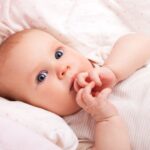 Bebeluș cu ochi mari, zâmbind, înfășurat în pătură moale.