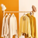O ținută de haine atârnate pe un suport, cu nuanțe calde de galben și crem.