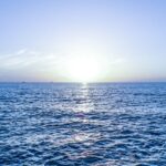 O mare calmă sub un cer senin, cu soarele răsărind la orizont.