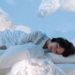 O femeie doarme liniștită pe un pat, înconjurată de nori pufoși.
