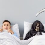 Un bărbat speriat stă în pat alături de o schelet cu coasa, simbolizând frica de moarte.