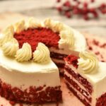 Tortă roșie cu cremă albă, feliată, pe o masă de lemn.