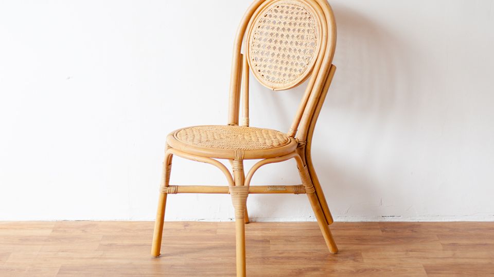 Un scaun din ratan cu un design elegant, așezat pe un fundal alb.