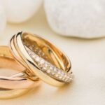 Trei verighete elegante, din aur roz și galben, strălucind pe un fundal de pietre albe.