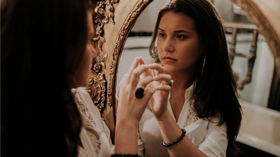 O tânără contemplându-se în oglindă, reflectându-și gândurile interioare.