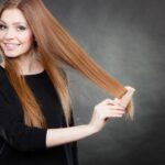 O femeie zâmbitoare își pieptănă părul lung, strălucitor, cu un pieptene.