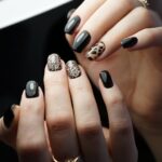 Mâini cu unghii negre și unghii cu model leopard, elegant și modern.