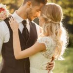 Un cuplu îndrăgostit se îmbrățișează într-un peisaj romantic, cu flori.